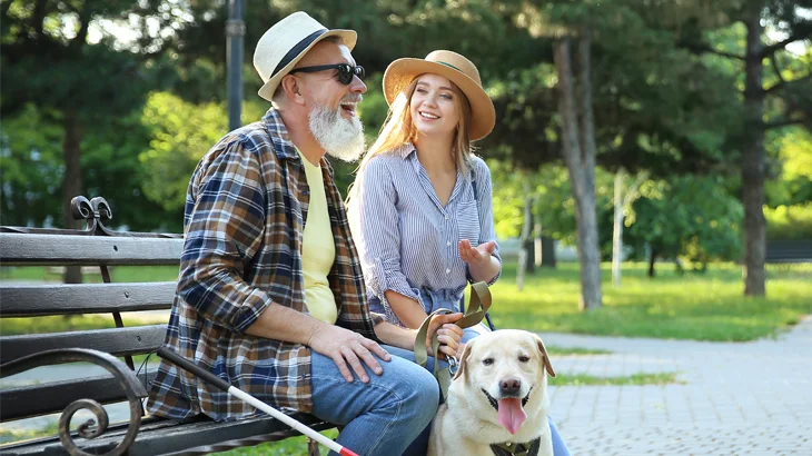 Homem com deficiência visual junto a um cão guia sentado no banco