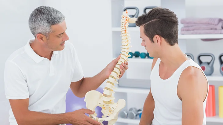 Homem segurando o protótipo de uma coluna vertebral ao lado de uma outro homem