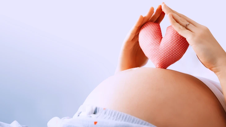 Mulher grávida segurando um coraçãozinho de pano