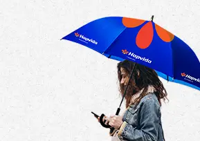 Uma mulher debaixo do guarda-chuva, mexendo no celular.