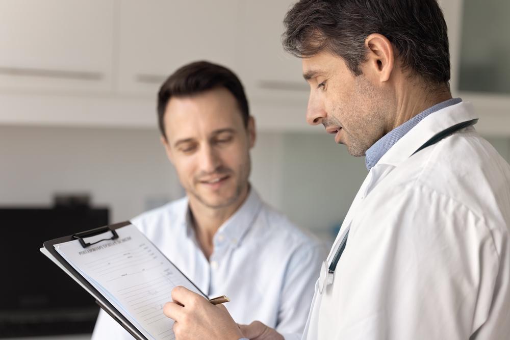 Quando procurar um urologista? Homem conversando com médico que aponta informações em uma prancheta, representando orientação especializada sobre fertilidade masculina.
