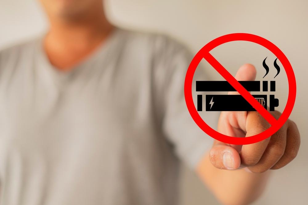 Como parar de fumar com segurança. Pessoa apontando para o símbolo de proibido fumar, com ícone de cigarro e vape riscados, reforçando a mensagem de combate ao tabagismo.