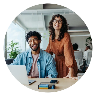 Dois colegas de trabalho sorriem ao lado de um notebook, transmitindo um ambiente descontraído e produtivo.